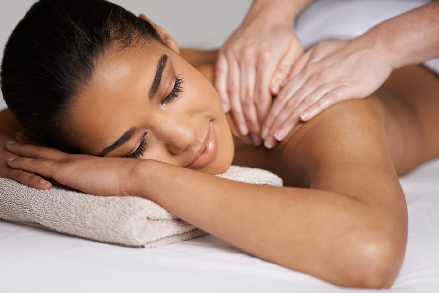 Femme souriante recevant un massage du dos, les yeux fermés et détendue sur une table de soin
